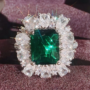 Macro shot of luxury emerald-cut green gemstone ring with white floral zircon halo