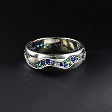 Dettaglio di un anello a onda d'argento con micro-pavé di pietre blu e verdi