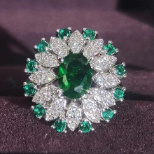 Detail of emerald oval center stone with shimmering petal diamond halo on silver band