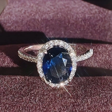 Close-up of an oval blue sapphire ring with a halo of small white diamonds in a velvet box