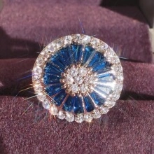 Top view of a round sunflower ring with blue baguette stones and micro-pave zircons