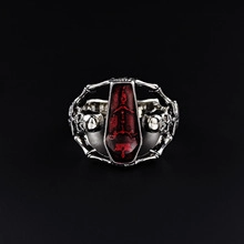 Macro detail of gothic coffin ring featuring silver skulls and red enamel center