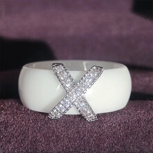 Close-up of a white ceramic wide band ring featuring a diamond-encrusted silver X-shape