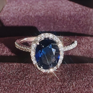Elegante anillo halo con piedra preciosa azul real ovalada y brillantes detalles de circón