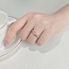 Detail of rose gold braided ring with pavé-set zircons held against a tea cup