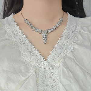 Detailed view of luxury zircon necklace with leaf-shaped pendant on white lace shirt