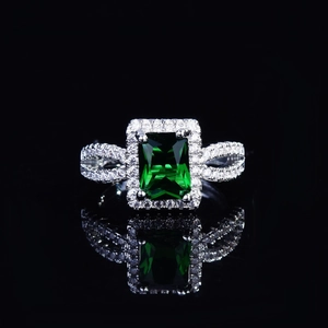 Luxuriöser Ring mit Smaragdschliff und Diamant-Halo auf schwarzer reflektierender Fläche