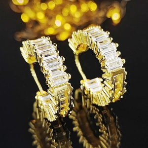Macro shot of gold C-shaped hoop earrings with baguette-cut cubic zirconia and warm bokeh light