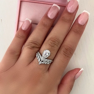 Dettaglio del set di anelli a corona con zircone a goccia su mano con sfondo rosa tenue