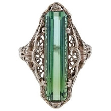 Macro view of vintage ring featuring emerald-cut green gemstone and hollow metal filigree