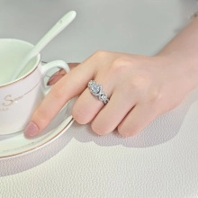 Close-up of a pear-cut halo diamond ring in silver worn on a finger beside a coffee cup