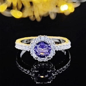 Macro shot of halo setting ring with purple round gemstone on a black reflective surface