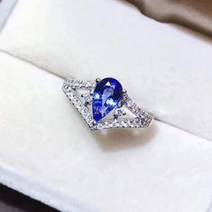 Elegant pear-cut blue gemstone ring with V-shape diamond halo in a white jewelry box