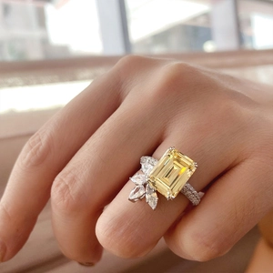 Close-up of emerald cut yellow gemstone ring with asymmetric diamond floral cluster