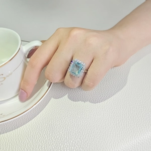 Detail eines luxuriösen rechteckigen blauen Edelsteinrings mit Halo-Diamanten am Finger