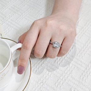 Macro shot of silver ring featuring square-cut halo diamond setting on woman's finger