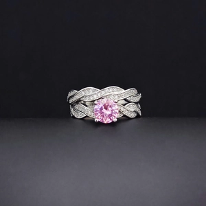 Macro view of braided silver band ring featuring a pink round gem and white pavé stones