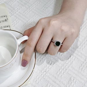 Detailed close-up of a silver ring with a halo-set square emerald green gemstone