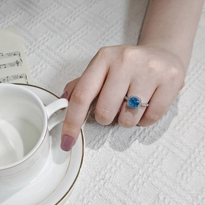 Elegant woman wearing square blue gemstone ring with halo diamonds at high tea setting