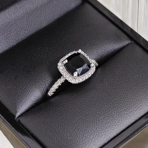Macro view of cushion-cut black gemstone ring with halo diamonds on a black leather box