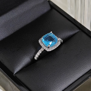 Macro shot of a luxury square blue gemstone ring with halo diamond setting on black box