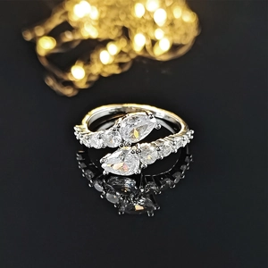 Macro shot of silver bypass ring with pear-cut zircon stones on reflective black surface