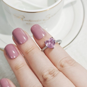 Nahaufnahme eines herzförmigen rosa Edelsteinrings mit Zirkonia-Akzenten an der Hand