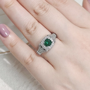 Detalle macro de mano con anillo de plata vintage, circón verde y piedras en pavé brillante