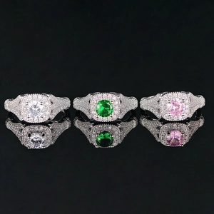Elegantes anillos de circón en blanco, verde y rosa sobre un fondo negro reflectante