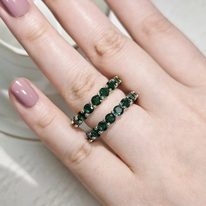 Close-up view of two emerald green zircon rings on finger with elegant purple nails