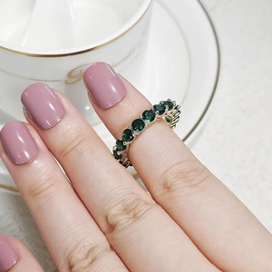 Close-up of gold eternity ring with round green zircon stones worn on finger