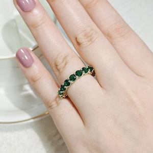Close-up of a gold ring with green emerald stones worn by a hand with purple nails