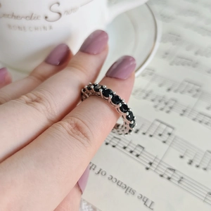 Close-up of silver eternity ring with black cubic zirconia and elegant lifestyle props