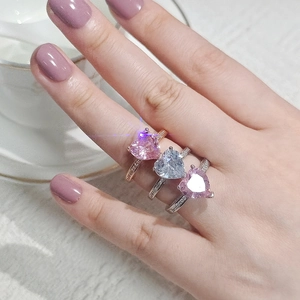 Close-up of heart-shaped pink and blue gemstone rings with diamond accents on model