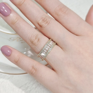 Close-up of elegant gold ring with emerald cut stones on a hand holding a white cup
