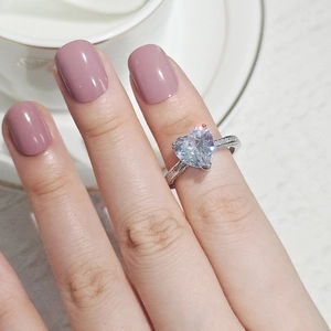 Close-up of a silver heart-shaped diamond ring with side accent stones on a female hand