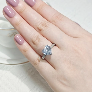 Close-up of heart-shaped diamond ring with pavé stones worn on a hand near a coffee cup