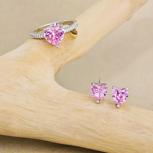 Nahaufnahme von rosa Herz-Zirkon-Schmuckset mit Ringen und Ohrringen auf Holzzweig