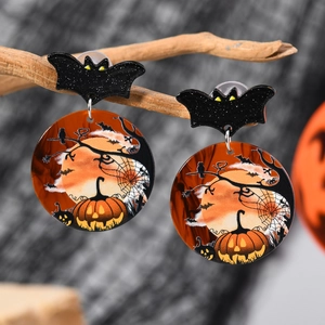 Halloween acrylic earrings with black bat stud and pumpkin moon pendant hanging on a dry branch