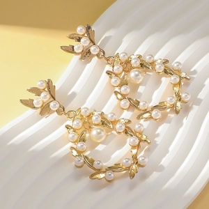 Détail de boucles d'oreilles nœud dorées avec incrustation de perles et pendentif