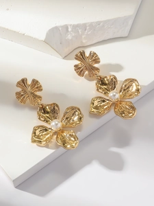 Détail de boucles d'oreilles fleurs dorées avec perles blanches sur fond géométrique