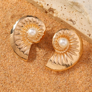 Boucles d'oreilles coquillage dorées avec perles sur fond de sable de plage au soleil