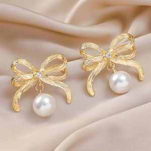 Élégantes boucles d'oreilles nœud doré avec perle blanche sur fond de satin champagne