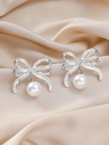 Détail des boucles d'oreilles nœud en métal brossé avec perle élégante et zircon