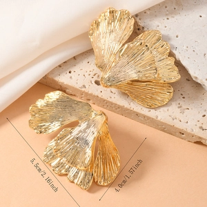 Macro shot of gold ginkgo leaf earrings with layered petals on stone and silk background