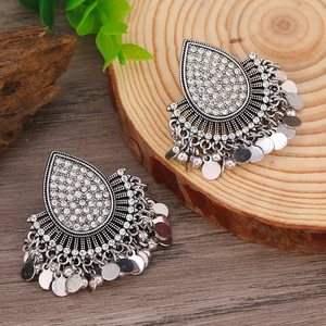 Dettaglio di orecchini boho a goccia con paillettes argentate su sfondo di legno naturale