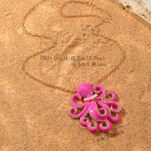 Macro-opname van de roze emaille octopus hanger met kristallen op een zandachtergrond