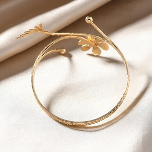 Golden flower and feather open bangle on elegant champagne silk background fabric