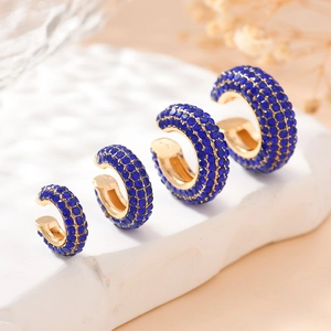 Détail de quatre bagues d'oreille dorées en forme de C serties de zircons bleus