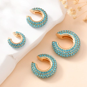 Lot de quatre earcuffs dorés en forme de C sertis de zircons bleus sur un support blanc